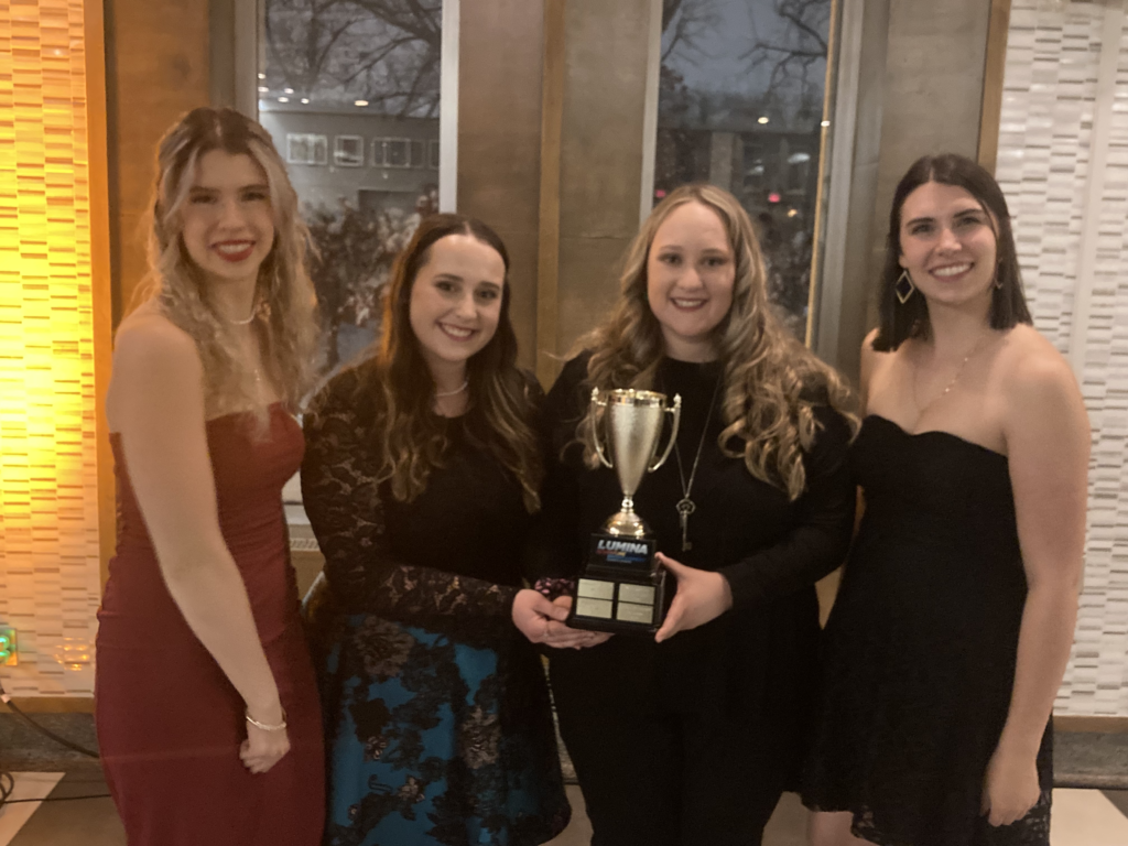 Past winners of The Agents of Cowl Murder Mystery: Sister Twins of VIDO. Four women in absolutely dashing attire smile for the camera while holding their trophy.