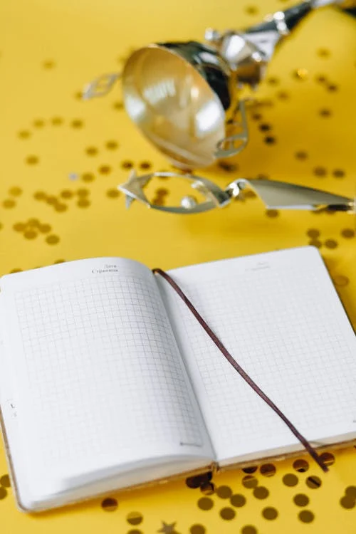 A notebook laying open on a yellow table with glitter and foil surrounding it.